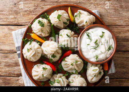 Georgian national dish khinkali dumplings with sour cream, pepper and herbs closeup on a plate on the table. Horizontal top view from above Stock Photo