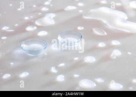 Contact lenses on white glass reflective table with water drops. Horizontal composition. Elevated view. Stock Photo