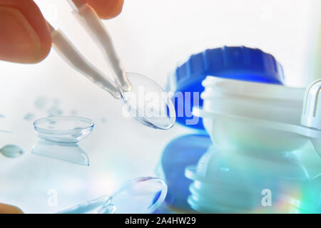 Manipulating a lens with white tweezers reflected on a glass table with water drops and lens case and  bluish background. Horizontal composition. Fron Stock Photo