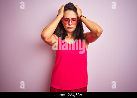 Beautiful woman wearing funny pink heart shaped sunglasses over pink isolated background suffering from headache desperate and stressed because pain a Stock Photo