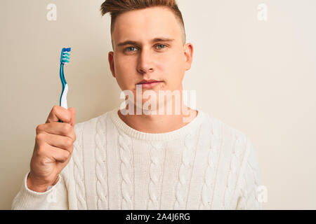 Young handsome man holding tooth brush standing over isolated white background with a confident expression on smart face thinking serious Stock Photo