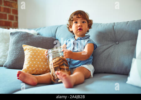 Beautiful toddler child girl holding jar of cookies sitting on the sofa Stock Photo