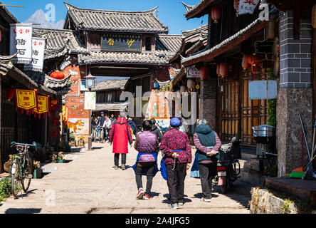 Baisha, China - February 11 2019: Local people walk toward the traditional Bai Sha Naxi village entrance gate near Lijiang in Yunnan province Stock Photo