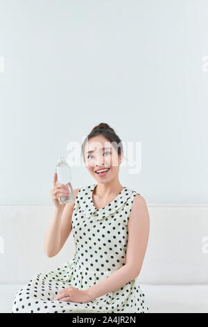 Happy girl holding a water bottle sitting on a couch in the living room Stock Photo