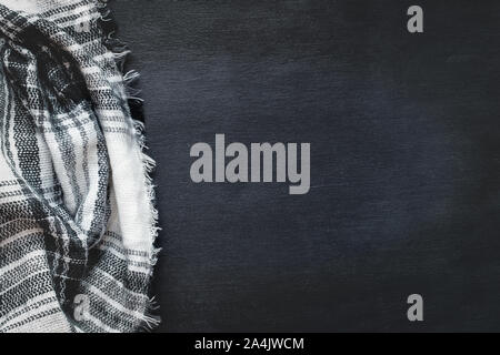 Warm woven black, white and gray blanket crumpled over a black wooden background. Shot from above top view with free space for text for background. Stock Photo