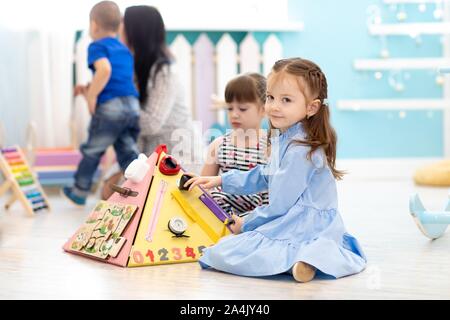 Cute toddler kid girl playing with busyboard in daycare. Children's educational toys. Stock Photo