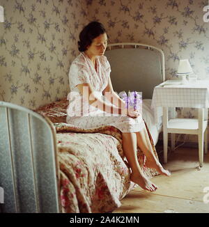 A barefoot woman sitting on the bed. Stock Photo