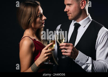 young elegant woman in red dress and handsome man in white shirt, tie enjoying spending time in the party, isolated black background, relationship. lo Stock Photo