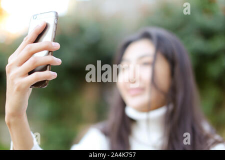 Focus on smartphone, blurred asian girl making selfie. Stock Photo