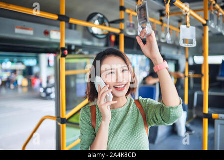 Beautiful young woman standing in city bus and talking on mobile phone. Stock Photo