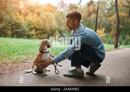 young handsome man teaching his dog to stand on two legs, paws, education, fulllength side view photo Stock Photo