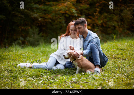Happy loving couple relaxing on grass stroking dog, full length photo. family, friendship Stock Photo