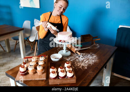 smiling beautiful professional confectioner using pastry bag in the kitchen. close up photo. spare time. Stock Photo