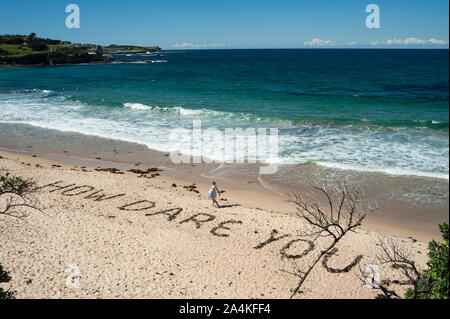24.09.2019, Sydney, New South Wales, Australia - A woman walks along Coogee Beach where the quote How Dare You? is written in the sand. Stock Photo