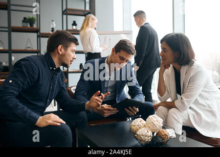 young business people discussing the positive and negative sides of problem, man holiding tabllet in hands, working with gadget Stock Photo
