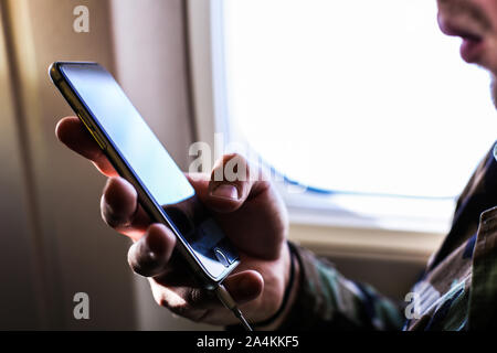 Closeup man using smartphone near window in airplane. Stock Photo