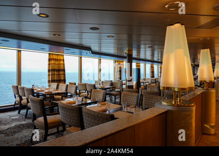 A dinner seating area on a cruise ship with big bright windows, gold