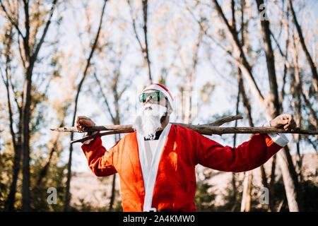 Santa Claus with sunglasses rest observing the forest with a branch on his shoulders Stock Photo