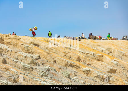 Java island, Indonesia - September 16, 2019: Basket laden by pieces of natural sulfur carrying by miner from crater mine. Extensive manual labour . Stock Photo