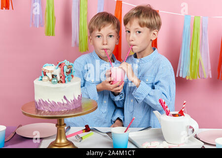 two funny little boys drinking juice at the party, isolated pink background, studio shot.