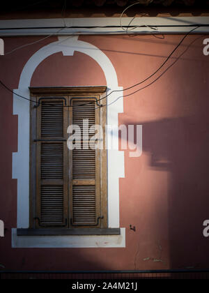 Morning light and shadow on the Red wall with rustic wooden shutter window. Stock Photo