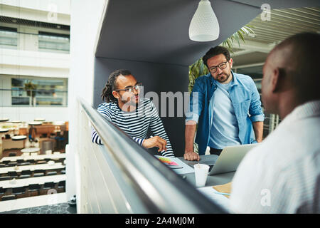 Diverse group of businessmen discussing work together in a meeting pod in the lobby of a modern office Stock Photo
