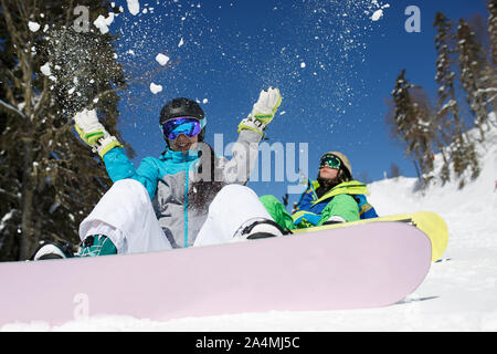 Woman in helmet throwing snow sitting next to man on hillside on winter day Stock Photo