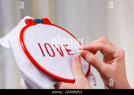 hands of woman embroidering a word love on canvas, closeup Stock Photo