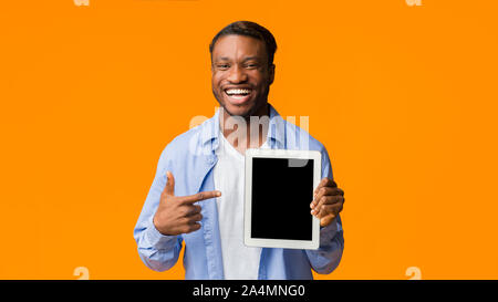 Black Guy Pointing Finger At Empty Tablet Screen, Orange Background Stock Photo