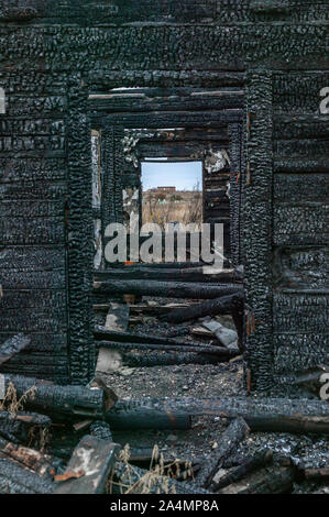 View from the window of a burnt wooden destroyed house in the cemetery. Mystical place. Vertical shot Stock Photo