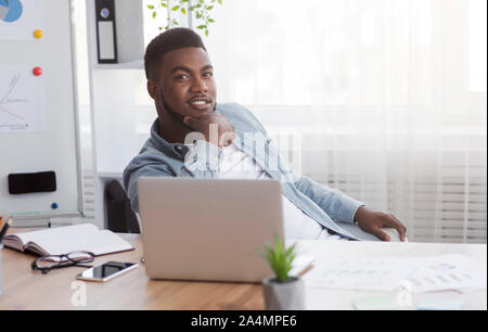 Young black entrepreneur sitting at workplace in his own office. Stock Photo