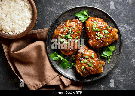 Honey grilled chicken thighs and bowl of rice over dark stone background. Tasty food in asian style. Top view, flat lay Stock Photo