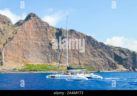 Madeira, Portugal - Sep 10, 2019: Tourist sightseeing boat with people in the waters of the Atlantic ocean. Rocks on Madeira island in the background. Whale watching, dolphin watching trips. Stock Photo