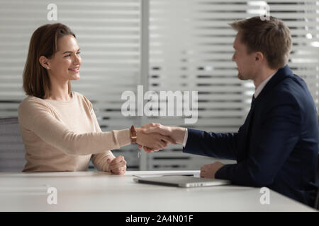 Confident businessman shaking hand of smiling businesswoman in office Stock Photo