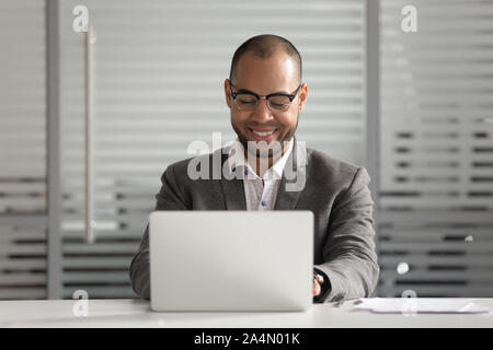 Smiling African American businessman using laptop, looking at screen Stock Photo
