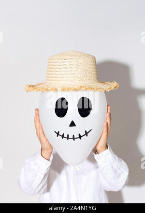 Woman holding ghost balloon in straw hat instead of her face Stock Photo