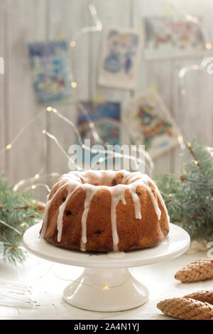 Pie with raisins and icing from powdered sugar on the background of fir branches and garlands. Rustic style. Stock Photo