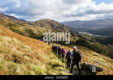 Ramblers group walking in a long line on a country path above Nant Gwynant in hills of Snowdonia National Park. Beddgelert, Gwynedd, north Wales, UK Stock Photo
