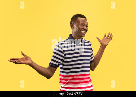 Nice to meet you. Young african-american man isolated on yellow studio background, facial expression. Beautiful male half-lenght portrait. Concept of human emotions, facial expression. Looking friendly. Stock Photo