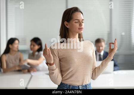 Mindful young businesswoman meditating, doing yoga exercise in office Stock Photo