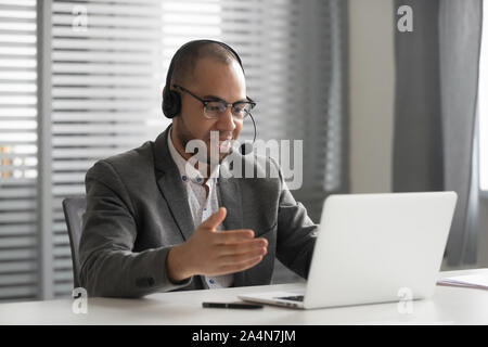 Smiling African American employee in headset using laptop, talking online Stock Photo