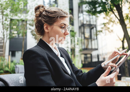 Happy business woman sitting at coffee shop working on digital tablet. Businesswoman at cafe on veranda using laptop computer. Stock Photo