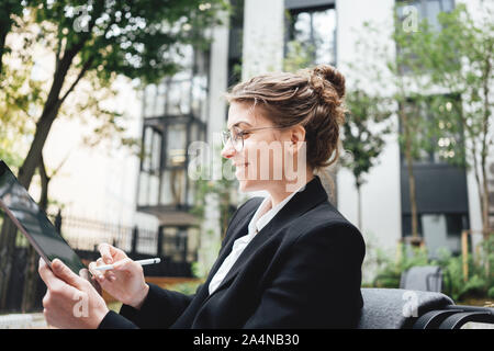 Happy business woman sitting at coffee shop working on digital tablet. Businesswoman at cafe on veranda using laptop computer. Stock Photo