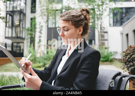 Businesswoman at cafe on veranda using gadgets for digital work. Young business woman sitting at coffee shop working on digital tablet. Stock Photo