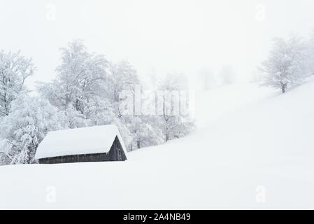 Snowy winter in a mountain village. Landscape with fog and deep snow. Lonely wooden house Stock Photo