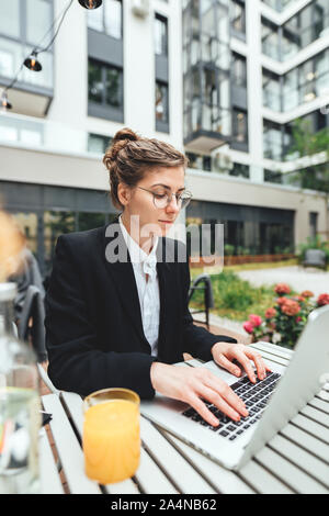 Young business woman wearing glasses at cafe using laptop and. Businesswoman sitting at coffee shop on terrace and working on computer Stock Photo
