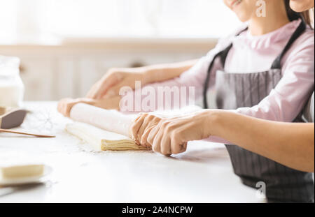 Woman helping child to roll out dough with rolling pin Stock Photo