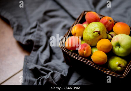 Fruit basket on grey tissu background. Fresh summer pears, apricots and apples Stock Photo