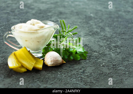 Tartar sauce in a glass gravy boat with ingredients on a black background. Copy space. Stock Photo