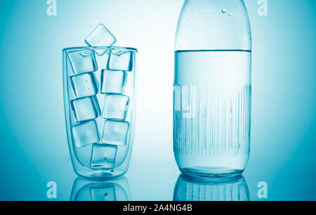 a glass with ice cubes and a bottle with fresh drink water on blue background Stock Photo